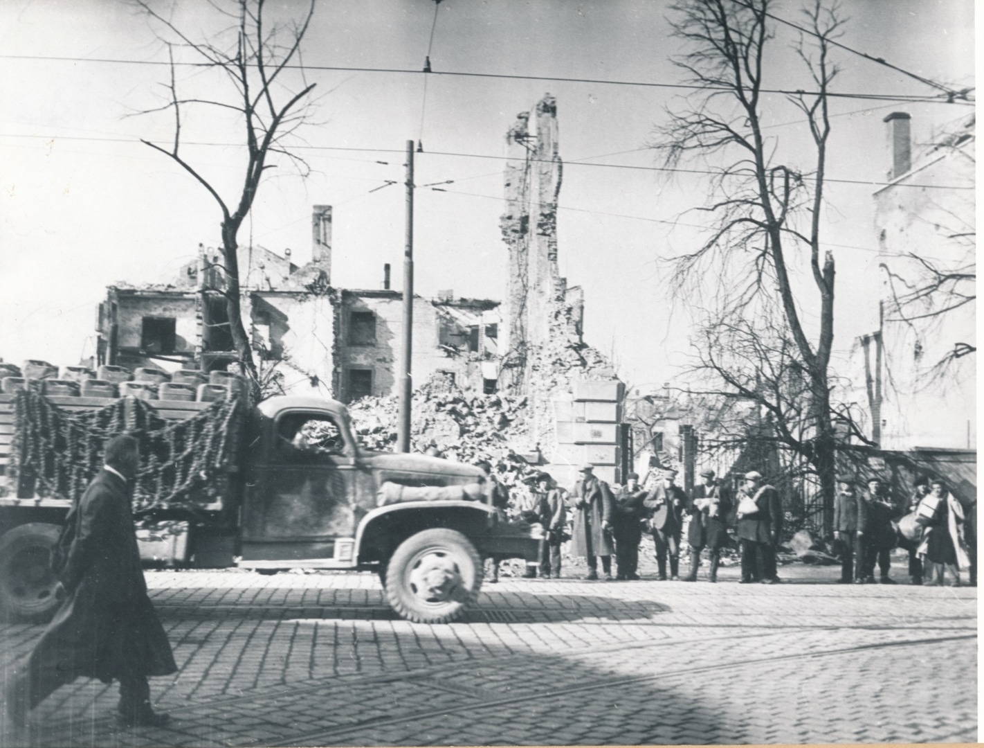 Befreite Zwangsarbeiter stehen am Rand der Rheinstraße (wohl gegenüber Einmündung Neckarstraße) und beobachten einen amerikanischen Truck, der in die Innenstadt fährt.